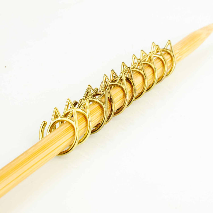 Row of gold cat-face stitch markers lined up on bamboo knitting needle