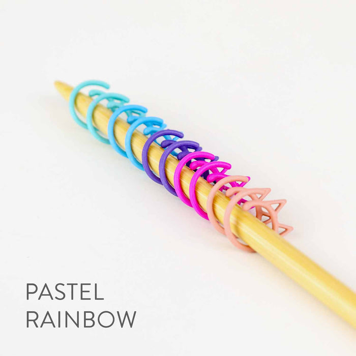 Ten pastel rainbow Cat Clip stitch markers on a bamboo knitting needle graduating from aqua to pink, labeled PASTEL RAINBOW