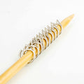 Ten silver cat-shaped removable stitch markers lined up on a bamboo knitting needle, showing the detailed cat-ear and tail silhouette design in metallic silver