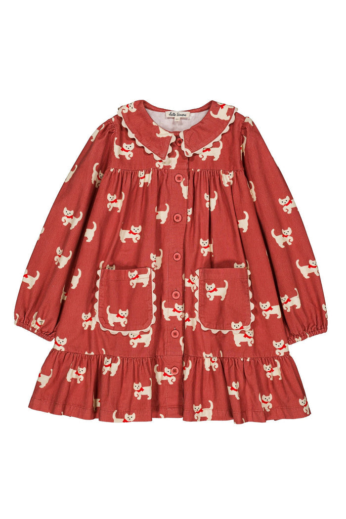 A child's long-sleeve button-up dress in a rust red fabric with a white cat print, featuring a Peter Pan collar, ruffled trim, and front pockets.