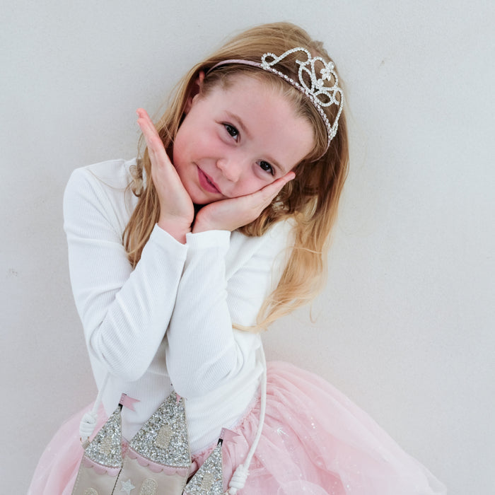 Young girl in a white top and pink skirt with a tiara on a plain background