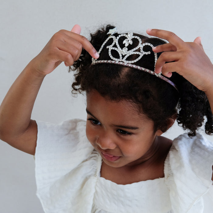 Child wearing a tiara with hands adjusting it against a plain background