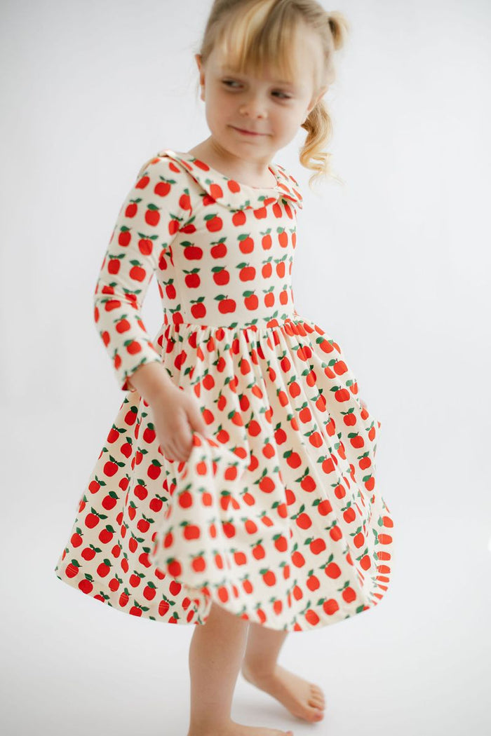 Young girl wearing a dress with red apple pattern on a white background
