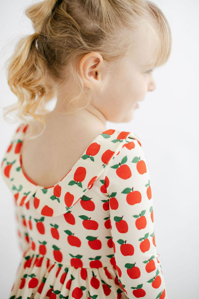 Child wearing a dress with red apple pattern on a white background