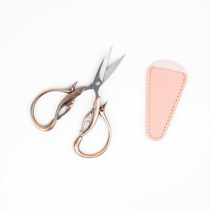 Copper swan embroidery scissors open with the pink leather blade cover showing the detailed wing design on the handles