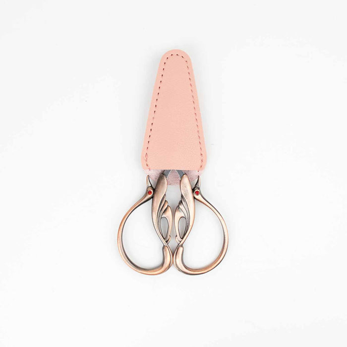 Copper swan embroidery scissors with blades tucked into the pink leather blade cover showing the swan handle design