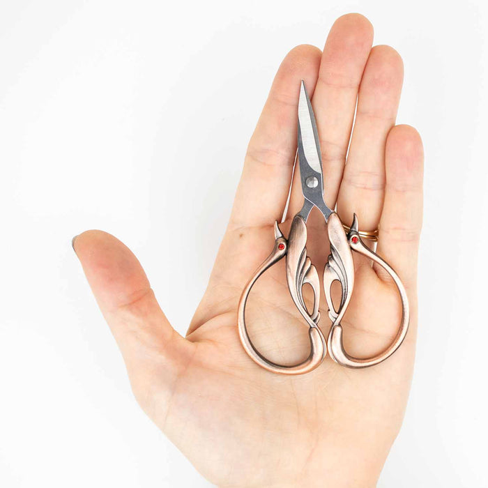 Hand holding the copper swan embroidery scissors to show the compact size and ornate swan-shaped handle detail