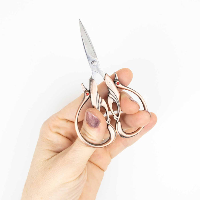 Hand gripping the copper swan embroidery scissors in cutting position to demonstrate comfortable use