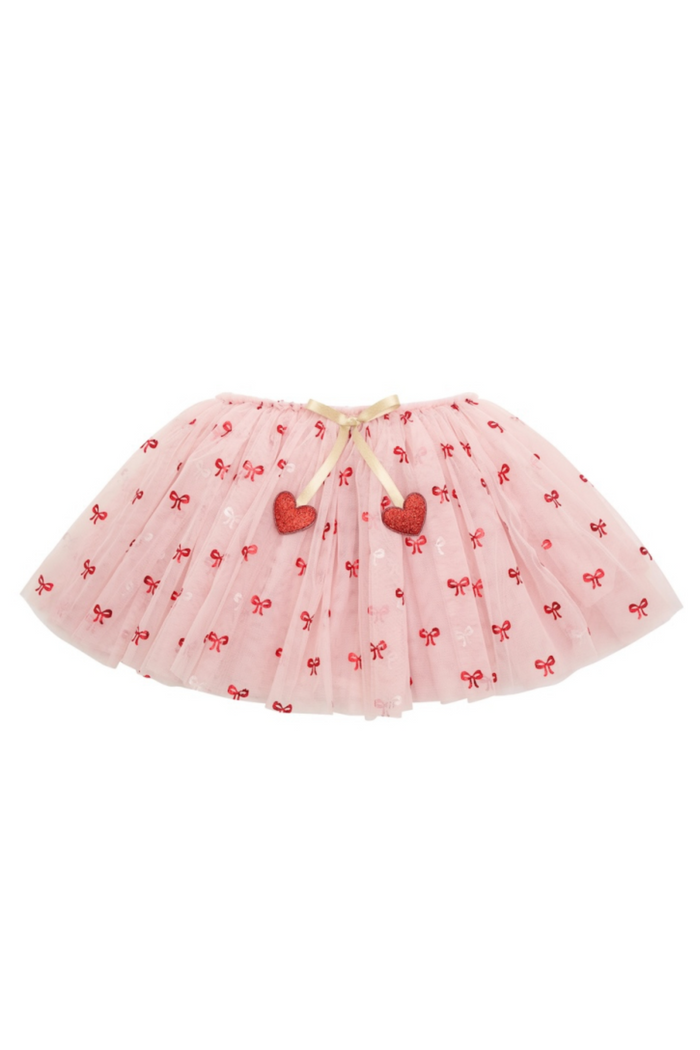 A light pink tulle tutu skirt decorated with small red bows and two red heart appliqués, tied with a beige ribbon at the waistband, shown on a plain white background.