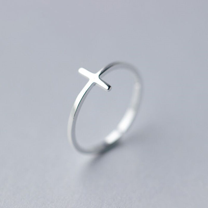 High-angle shot of a polished silver-tone sideways cross ring featuring a sleek, open-ended adjustable band design on a white background.