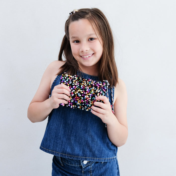 Young girl holding a colorful clutch against a plain background