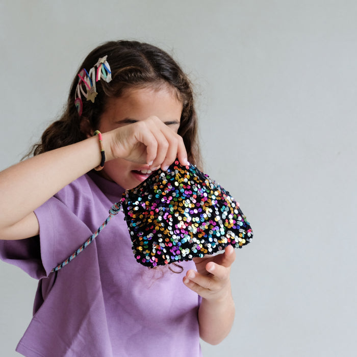 Child holding a colorful sequin bag against a plain background