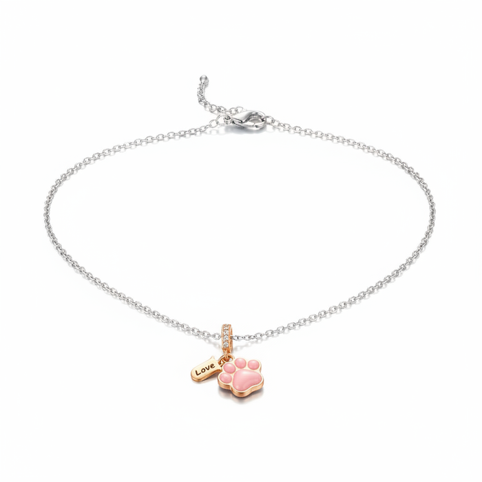A delicate silver-toned chain anklet featuring a rose gold-trimmed pink enamel paw print charm and a small 'Love' engraved tag, isolated on white.