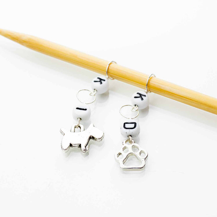 Dog charm increase and decrease stitch marker set on wooden knitting needles, showing silver dog, bone, paw print, K, I, and D letter charms
