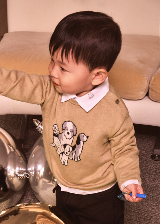 Child wearing a beige sweater with dog illustrations in a living room setting