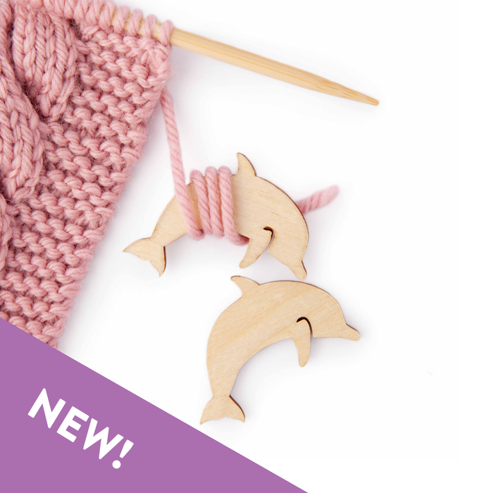 Wooden dolphin-shaped knitting markers with pink yarn and a purple banner on a white background
