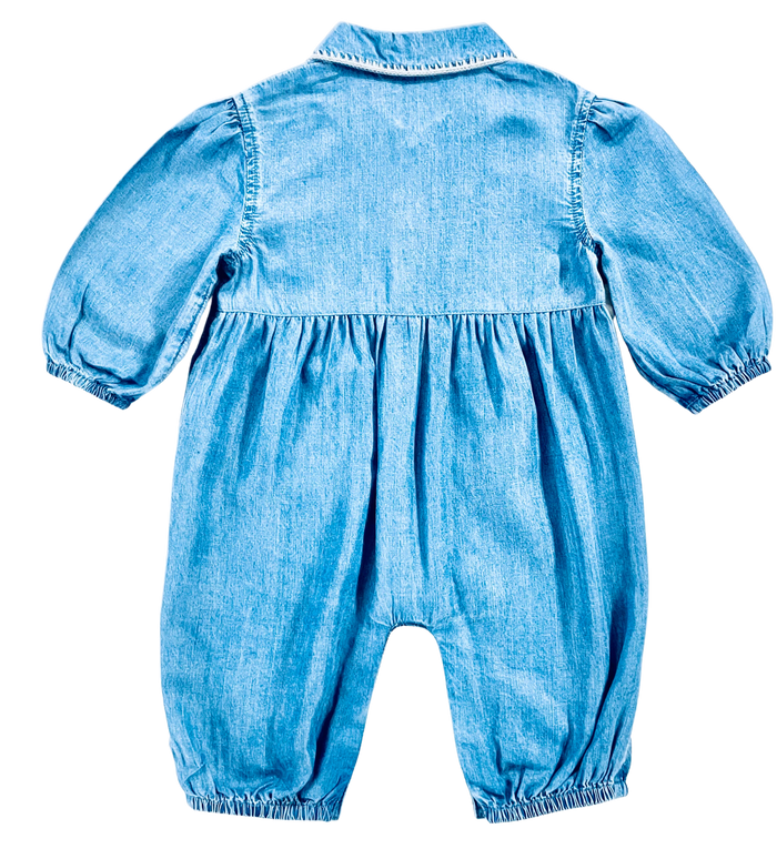 A baby romper in light blue chambray fabric, shown from the back against a plain white background.