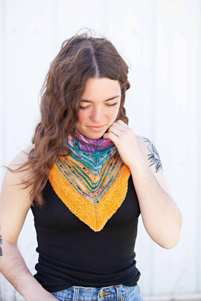 Model wearing the Down By The Sea shawl as a bandana cowl at the neck, front view showing the chevron point in magenta, teal, and gold