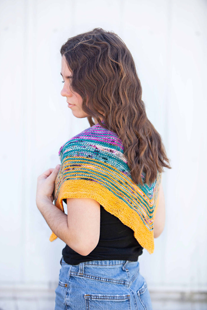 Side profile of model wearing the Down By The Sea shawl draped over one shoulder, showing the drape and color gradation from magenta to teal to gold