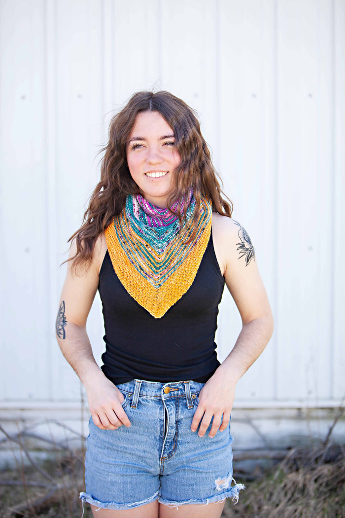 Model smiling and wearing the Down By The Sea shawl as a bandana cowl with a black tank top and denim shorts, casual summer styling