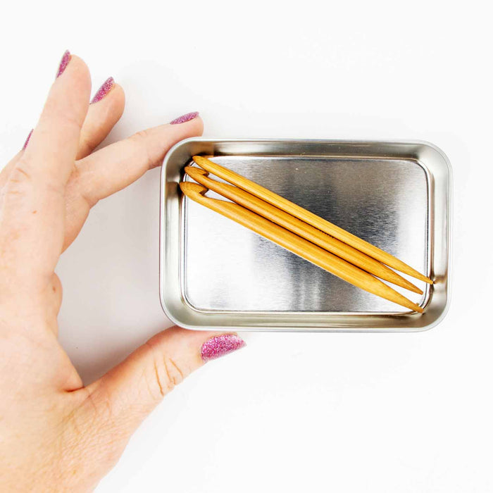 Hand holding an open silver tin containing three Duo wooden repair hooks showing the compact storage size
