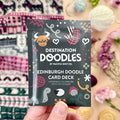Hand holding the Edinburgh Destination Doodle Card Deck foil pack by Pacific Knit Co