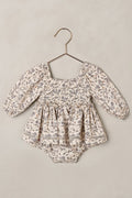 Baby romper with floral pattern on a hanger against a beige background