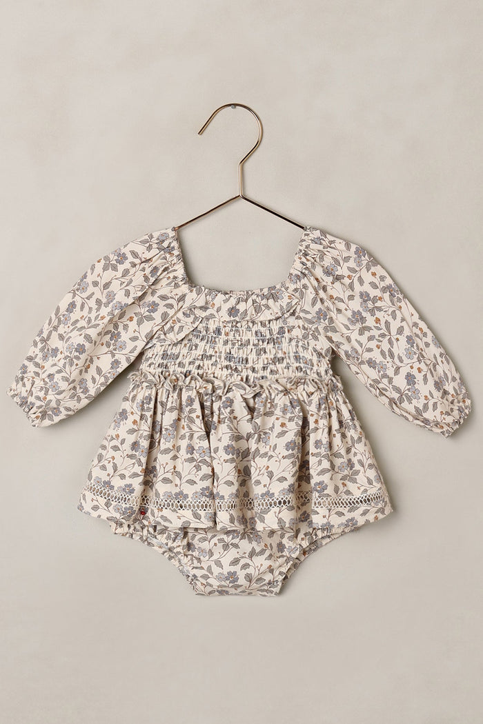 Baby romper with floral pattern on a hanger against a beige background