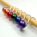 Rainbow pearl infinity ring stitch markers in orange, pink, green, blue, and purple on bamboo knitting needle