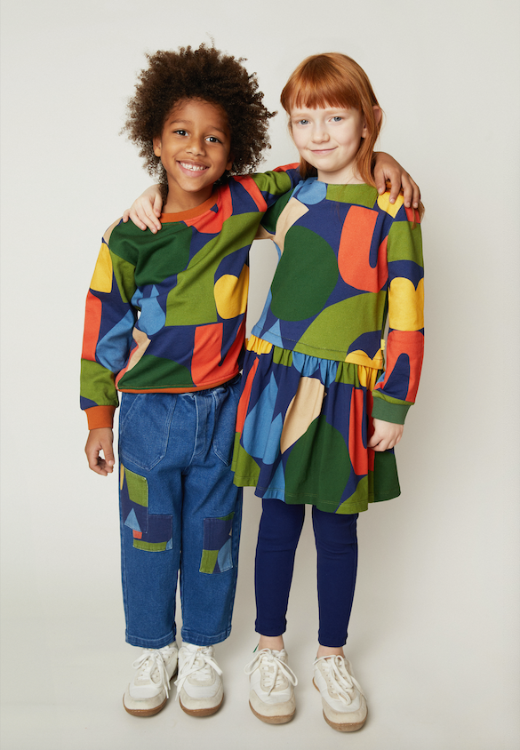 Two children modeling matching colorful abstract print sweatshirts and jeans against a plain light gray studio background.