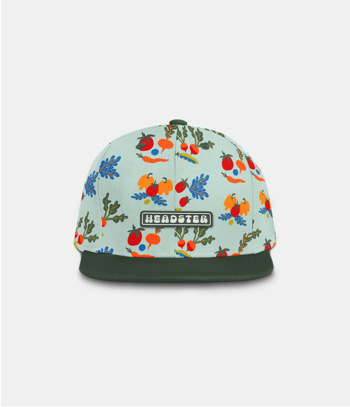 A snapback cap with a mint green background and a colorful botanical pattern of berries, leaves, and flowers. It features a dark forest green flat brim and a green and white 'HEADSTER' patch on the front.