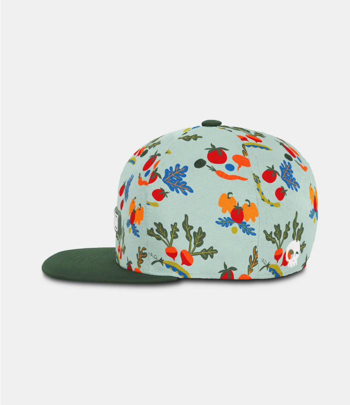A snapback cap with a light blue-green background and a colorful vegetable print on the crown, paired with a solid dark green flat brim.
