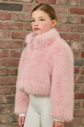 Young girl wearing a pink fluffy jacket against a brick wall.