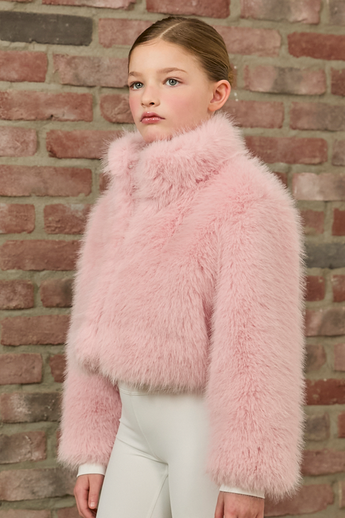 Young girl wearing a pink fluffy jacket against a brick wall.