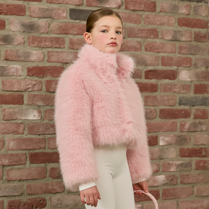 Child wearing a pink fluffy coat against a brick wall