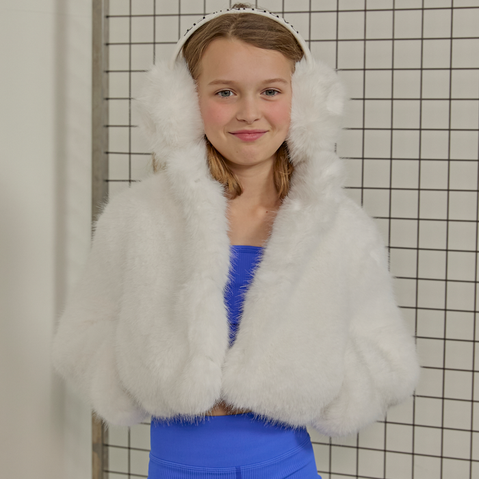 Young girl wearing a white fluffy coat against a tiled wall.