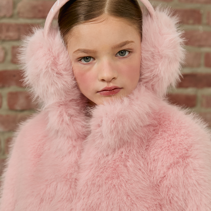 Person wearing a pink fluffy earmuffs against a brick wall
