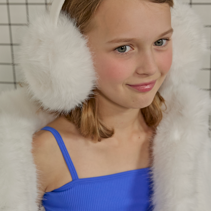 Young girl wearing white fur earmuffs and a blue top against a neutral background