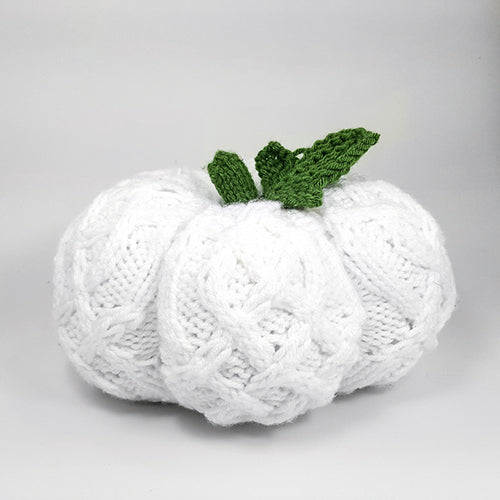 White cable-knit pumpkin with green knitted stem and leaf showing the textured cable stitch pattern from the front