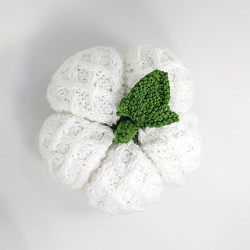 Top-down view of the white cable-knit pumpkin showing the segmented cable pattern and green knitted stem and leaf