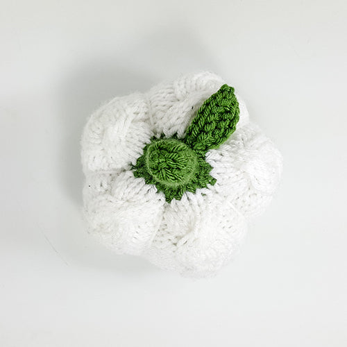 Top-down view of the white cable-knit pumpkin showing the ribbed segments and green knitted leaf detail