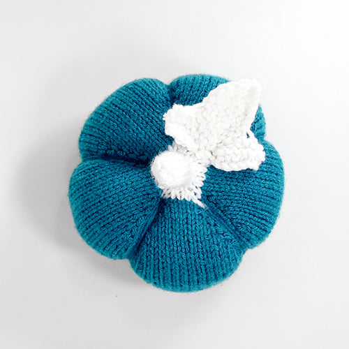 Top-down view of the teal ribbed-knit pumpkin showing the segmented ribs and white knitted stem and leaf