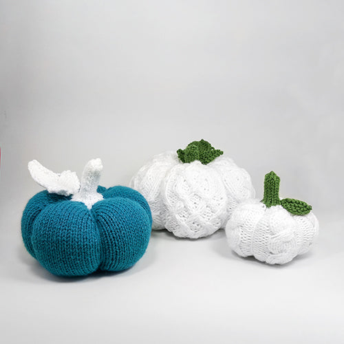 Three festive knitted pumpkins arranged together in teal ribbed and white cable patterns in small, medium, and large sizes