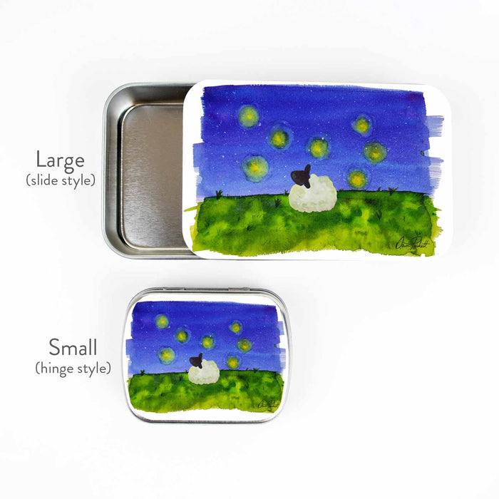 Firefly Dreams storage tin side-by-side size comparison showing the large slide style and small hinge style, both featuring the watercolor sheep and fireflies night scene by Dawn Prickett
