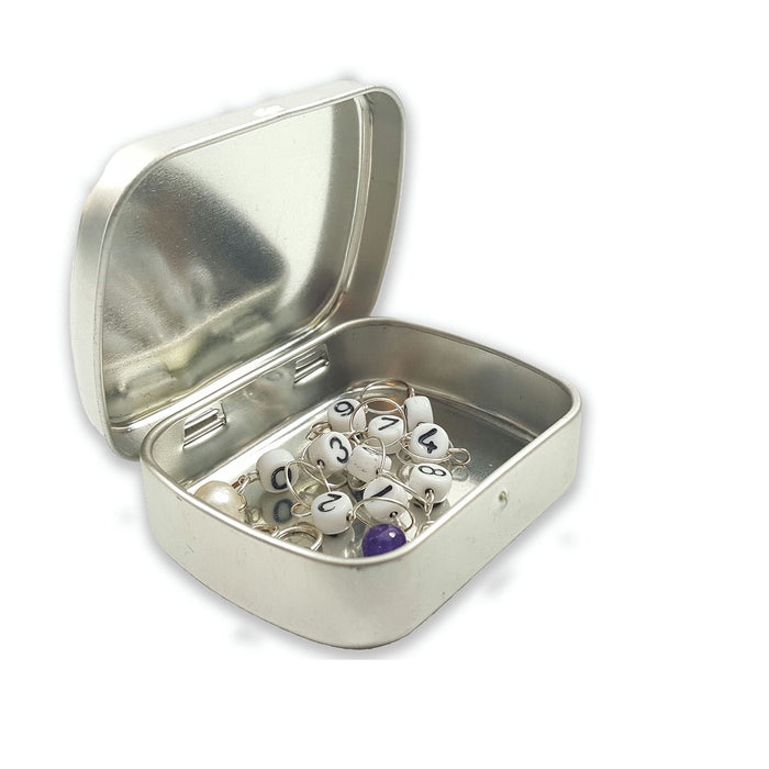 Open storage tin with X-shaped divider showing organized stitch markers and knitting accessories in compartments
