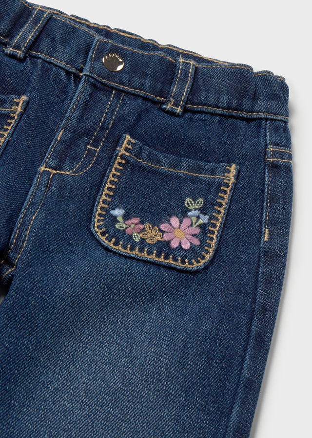 Close-up of blue denim pants with floral embroidery on a white background