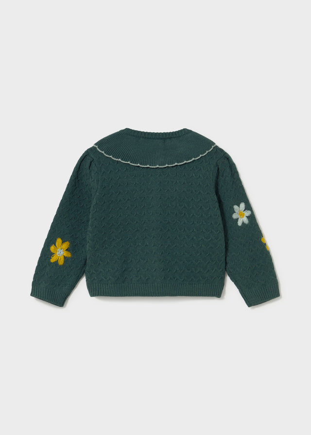 Green knitted cardigan with floral patterns on a light gray background