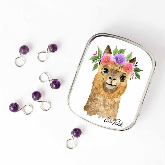 Small hinge-style Flower Alpaca storage tin open beside purple amethyst bead infinity-loop snag-free stitch markers on white background