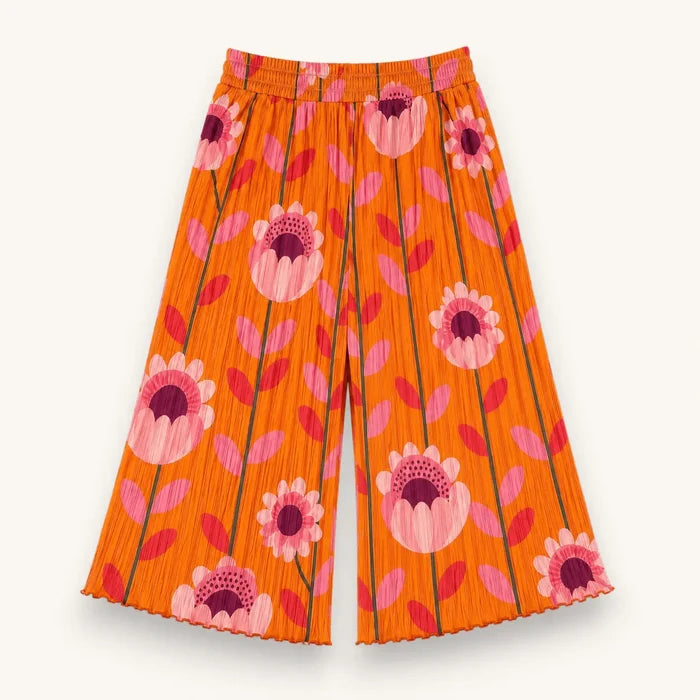 Orange pleated wide-leg pants with a retro floral print in pink, magenta, and purple, shown flat against a light off-white background.