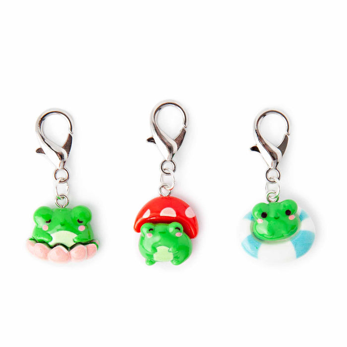Three cute frog lobster-clasp stitch markers featuring a green frog sitting on a pink lily pad, a frog wearing a red polka-dot mushroom cap hat, and a frog floating in a blue and white striped pool ring